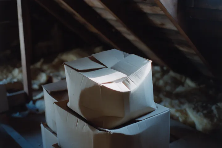 Folded cardboard boxes stacked in an unfinished attic under a gable vent.